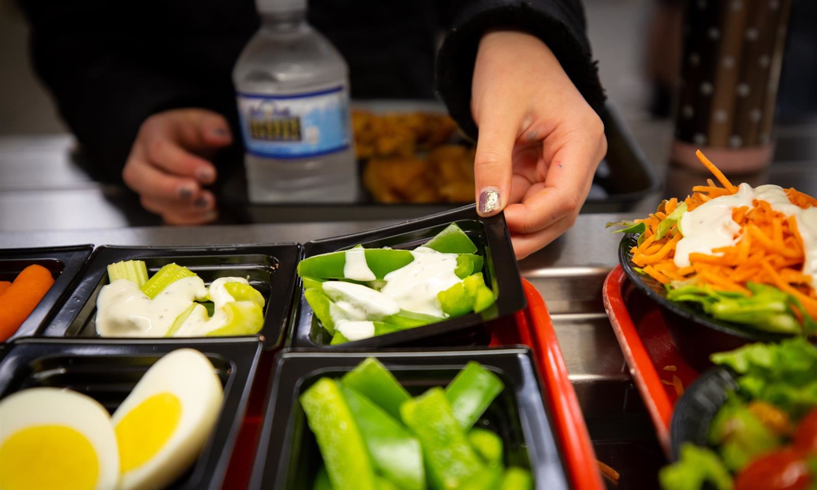 Student picking up a lunch tray item of veggies 
